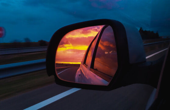 Nubes de atardecer reflejadas en el espejo retrovisor de un choche por la autopista