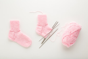Pink socks, wool clew and needles on white table background. Closeup. Preparing child warm knitted...