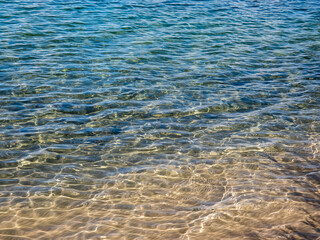 Texture of crystal clear light blue and turquoise transparent water with fine white sand base with bright reflection of sun in water movement. Water background