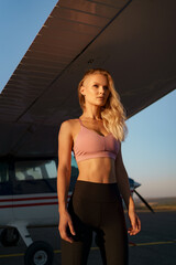 Young woman model with a modern haircut posing near a red plane wearing trendy sport outfit