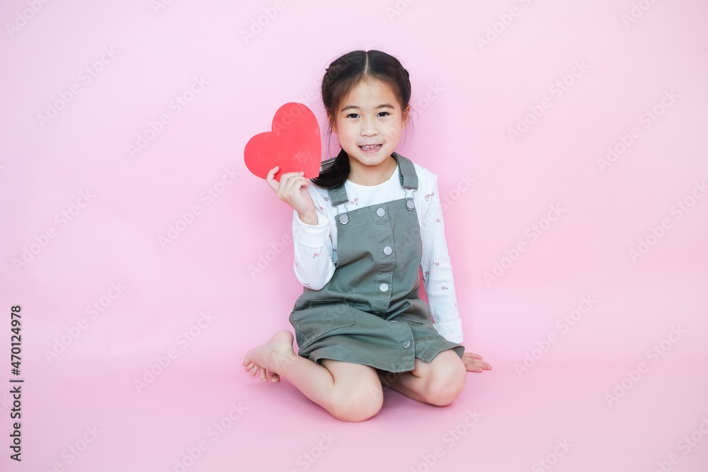 Wall mural portrait beautiful cute asia child girl on pink background with red heart sign, valentine day in lov