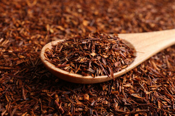 Heap of dry rooibos tea leaves with wooden spoon, closeup view