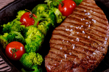 Grilled medium rare beef chop with sea salt, broccoli and tomato on grill pan.
