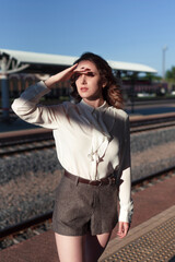 A young beautiful woman in a white shirt stands on the platform of the railway station, looks into the distance seeing off or meeting. The woman is waiting.