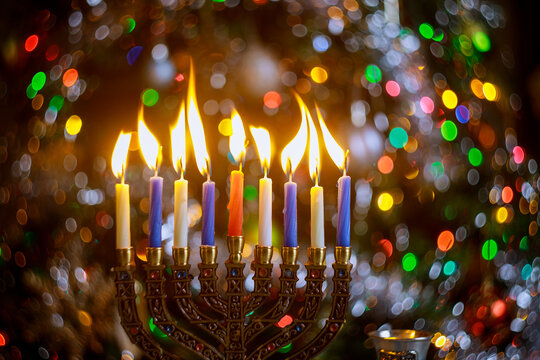 Burning candles on menorah for Hanukkah on defocus color lights background.