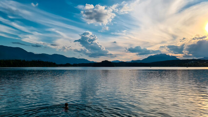 A woman swimming in the Lake Faak in Austria. The lake is surrounded by high Alpine peaks. The sun...
