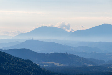 A panoramic view on endless mountain chains in Carinthia, Austrian Alps. The mountains are shrouded in fog. In the distance you can see the viewing tower Pyramidenkogel. Serenity and calmness