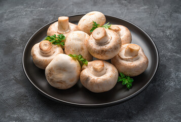 Fresh mushrooms and parsley in a black plate on a dark background.