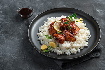Spicy teriyaki chicken in sweet and sour sauce with rice on a dark background.