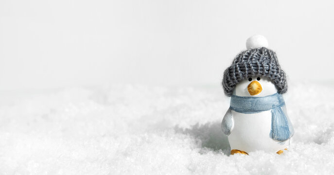 Christmas white snow background, panorama. Happy cute penguin in a winter hat on snowdrifts with hard shadows on the snow. Christmas or New Years concept. Bird penguin in a snowdrift. Banner