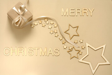 A gift wrapped in natural paper and a satin ribbon on a beige background decorated with wooden stars. Christmas inscription made of wooden letters.