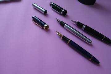 Collection of fountain pens on coloured texture pink background. office work, writing.
