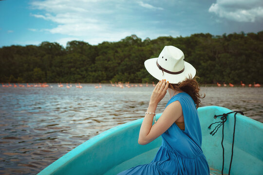 A young woman tourist in a boat watches pink flamingos in the Celestun National Park in Mexico. Flamingo birds at Ria Celestun Biosphere Reserve, Mexico