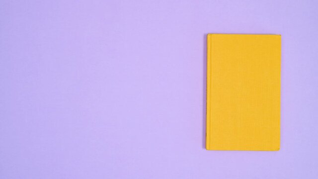 Yellow hardcover retro vintage book move left right on purple theme. Stop motion flat lay