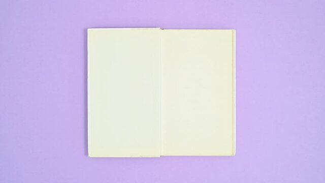 White hardcover opened book appear on purple theme, close and open again. Stop motion flat lay