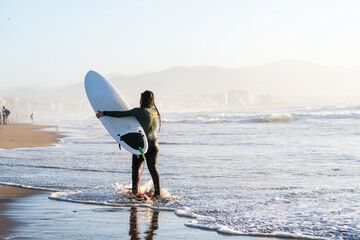 young female surfer walking on the beach holding surfboard in La Serena Chile	