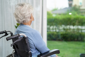 An elderly woman sitting on wheelchair looking out the window for waiting someone. Sadly,...