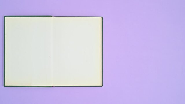 Hand put dark green hardcover retro vintage book on purple theme and book opens. Stop motion flat lay