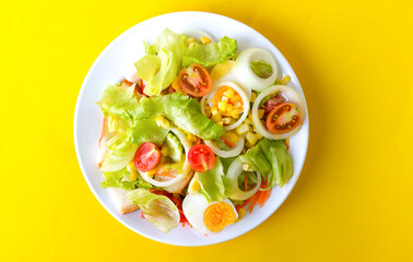 Delicious fresh vegetable salad on a white bowl on yellow background, top view.