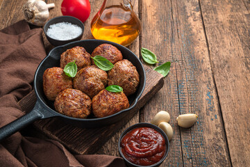 Fried meatballs with spices and sauce on a wooden background.