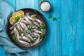 Sprat in a black plate with lemon and parsley on a blue background.