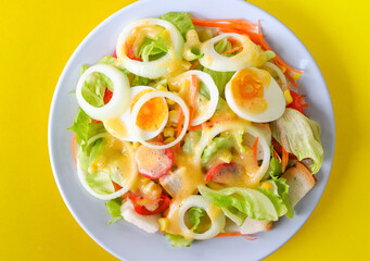 Delicious fresh vegetable salad on a white bowl on yellow background, top view.