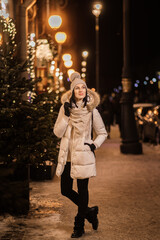 beautiful young woman in warm clothes near the Christmas tree in the lights on the city street and blurry lights in the background