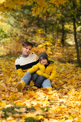 Fototapeta premium Happy young mother and little son sitting in autumn park among the yellow maple leaves