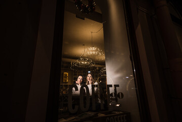 two beautiful young women are sitting at a table in a cafe. view through the window with the inscription coffee to go