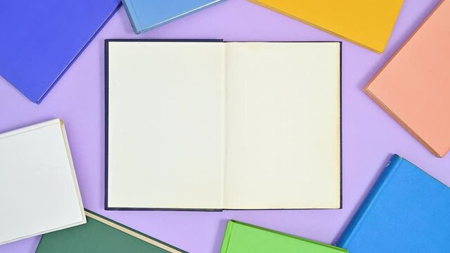 Deep blue hardcover book appear on purple theme and opens and vibrant colors books appear around make frame. Stop motion flat lay