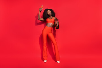 Full size portrait of pretty positive lady hold sparkling wine have fun retro celebrate holiday isolated on red color background