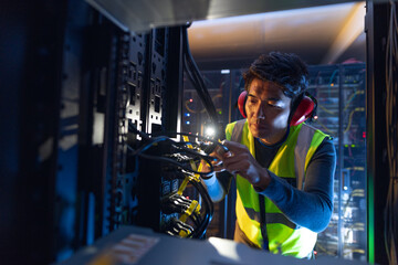 Asian male engineer using smartphone flash while inspecting the server in computer server room
