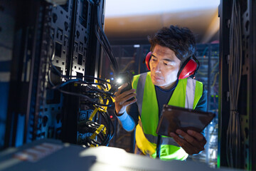 Asian male engineer using smartphone flash while inspecting the server in computer server room