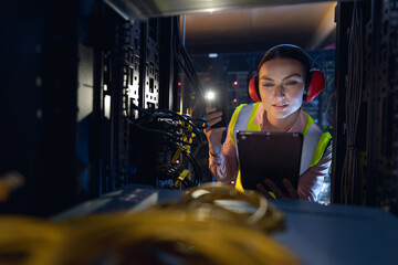 Caucasian female engineer using smartphone flash while inspecting the server in computer server room