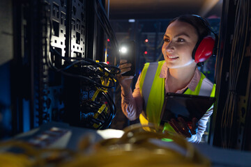 Caucasian female engineer using smartphone flash while inspecting the server in computer server room