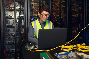 Asian male engineer using a laptop in computer server room