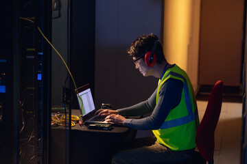 Asian male engineer wearing ear plugs using a laptop in computer server room