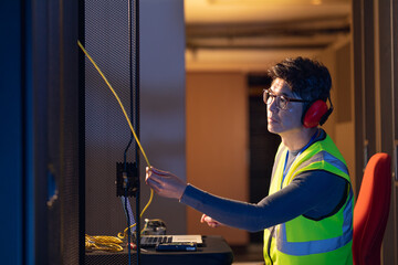 Asian male engineer wearing ear plugs touching a wire in computer server room