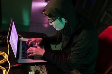 Asian male hacker using a laptop in computer server room