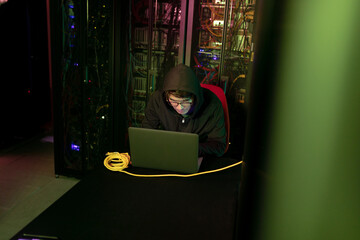 Asian male hacker using a laptop in computer server room