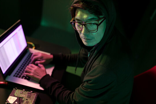 Asian male hacker using a laptop in computer server room