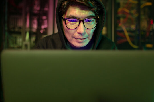 Asian male hacker using a laptop in computer server room