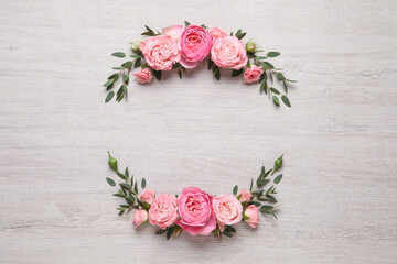 Wreath made of beautiful rose flowers and green leaves on white wooden background, flat lay. Space...