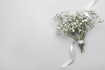 Beautiful bouquet of white gypsophila flowers with ribbon on light grey background, top view. Space...