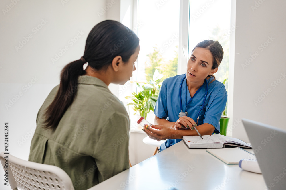 Wall mural White woman doctor talking with patient while working in her office