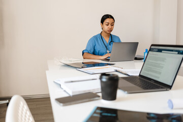 Hispanic woman doctor typing on laptop while working in office