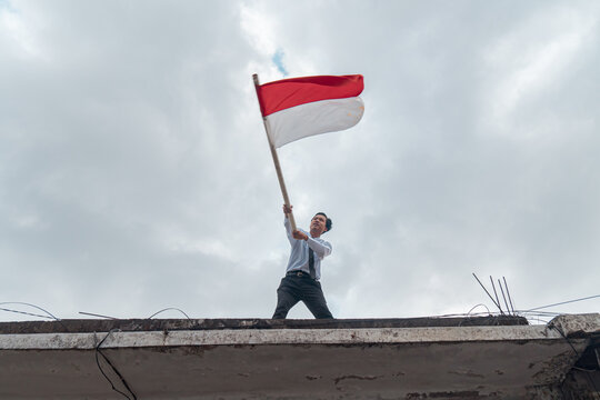 A man in neat clothes is commemorating Indonesia's independence day on August 17 by flying the red and white flag above the balcony
