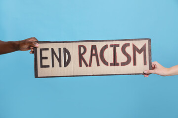Woman and African American man holding sign with phrase End Racism on light blue background, closeup