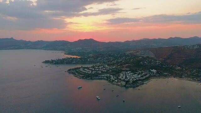 Aerial drone view of district of Bodrum Bitez at beautiful sunset, bay with boats in Aegean sea, town with beautiful low-rise houses mountains in background