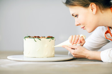 Confectioner finishing carrot cake with pastry bag, close-up on woman's hands and face. 